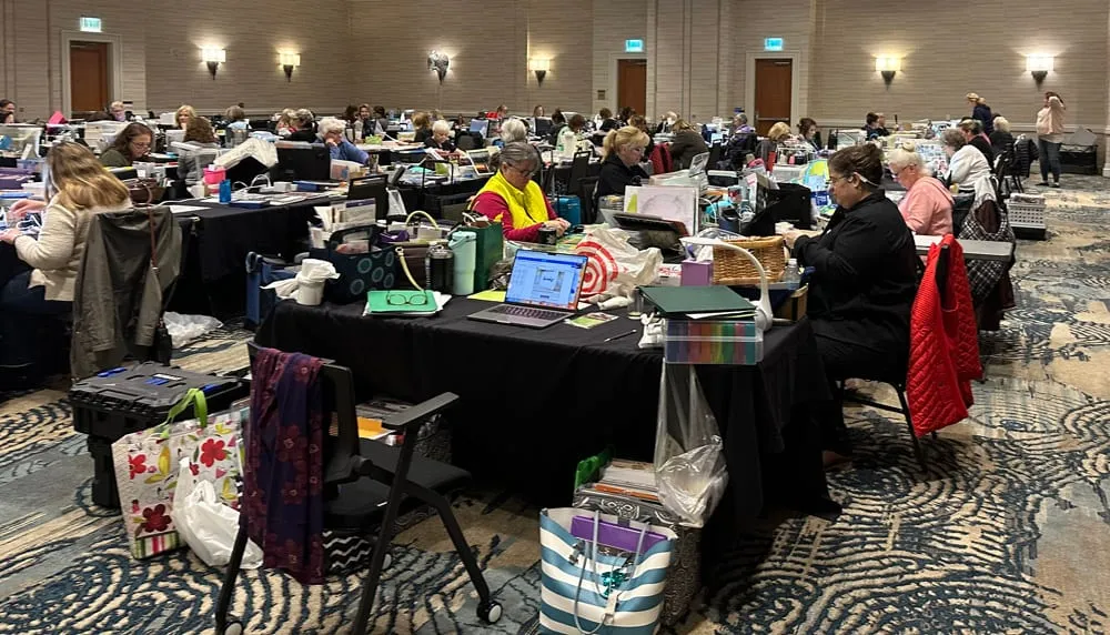 A hotel ballroom full of croppers at their tables, heads down over layouts and laptops